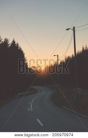 Empty lonesome suburb countryside road with woods silhouettes.