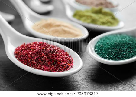 Maqui berry and spirulina powders in white ceramic spoons on black background