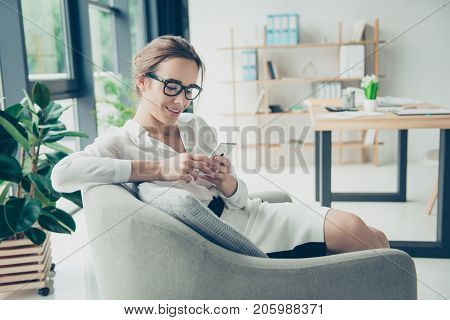 Comfort And Cozy Place. Young Cute Lady In Black Trendy Eyewear Is Browsing On Her Phone, Sitting On