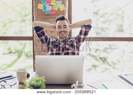 Cheerful Young Brunet Guy Is Resting In Front Of His Laptop Screen, At His Work Place, With Arms Beh