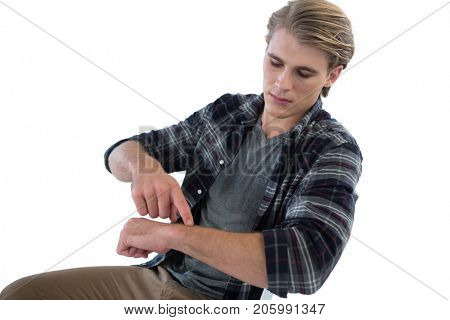 Young businessman looking at imaginary wristwatch while sitting on chair against white background