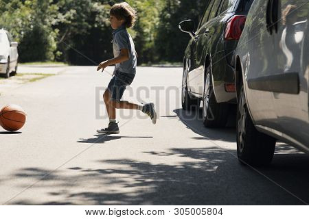 Careless Boy Running Behind The Ball On The Road Next To Cars