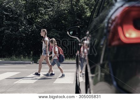 Low Angle On Car In Front Of Children With Backpacks Walking Through Crosswalk To The School
