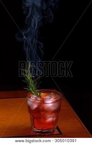 Rosemary Smoked Negroni Cocktail. Negroni Cocktail Glass On Wooden Table With Branch Smoking Rosemar