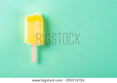 Yellow Popsicle With Couple Of Bites On A Light Green Background
