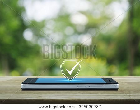 Security Shield With Check Mark Icon On Modern Smart Mobile Phone Screen On Wooden Table Over Blur G