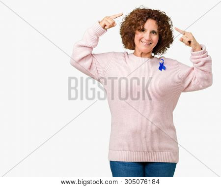 Middle ager senior woman wearing changeable blue color ribbon awareness over isolated background Smiling pointing to head with both hands finger, great idea or thought, good memory