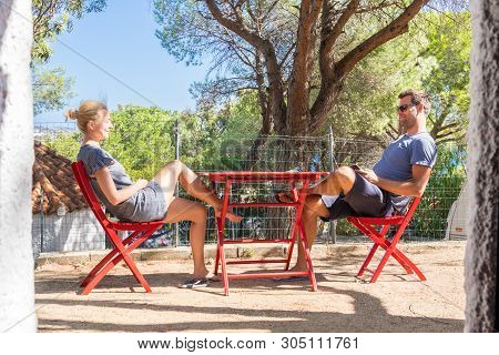 Couple On Vacations Resting In Front Of Bungalow House At Camping Site In Pure Nature. Family Vacati