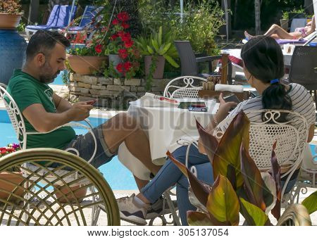 Cyprus - May 31, 2019: Young Couple Relaxing Sitting At A Table In An Outdoor Restaurant With A Pool