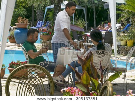 Cyprus - May 31, 2019: Young Couple Relaxing Sitting At A Table In An Outdoor Restaurant With A Pool
