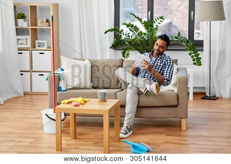 household and time management concept - smiling indian man making to do list in notebook after home cleaning