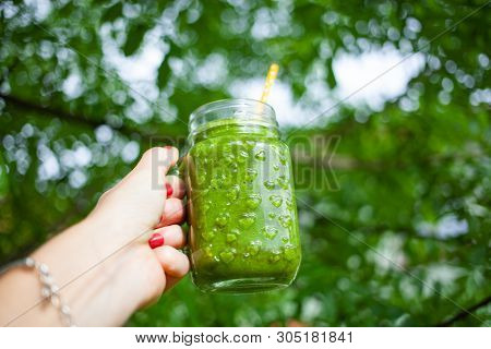 woman's hand holding a jar with green cold-pressed juice, nature background. Healthy eating, detoxing, juicing, body cleancing concept 