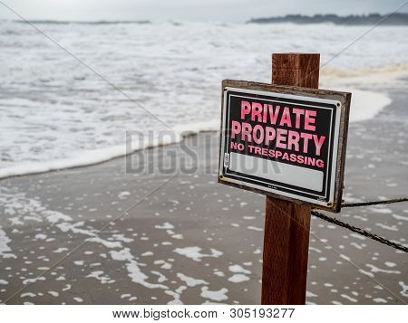 Private Property No Trespassing Sign On Pole And Wire Fence On A Beach Property Next To Waves