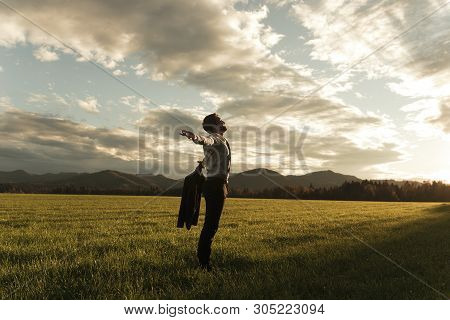 Successful Young Businessman Standing Under Glorious Cloudy Sky Lit By The Evening Sun With His Arms