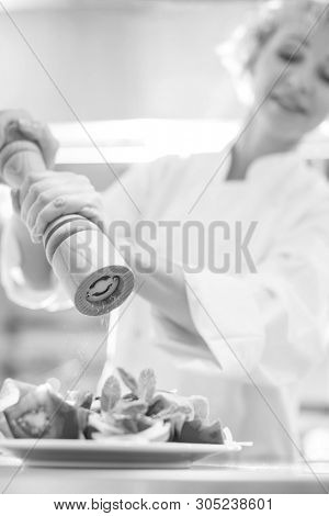 Black and White photo of Mature chef using peppermill on salad in plate at restaurant