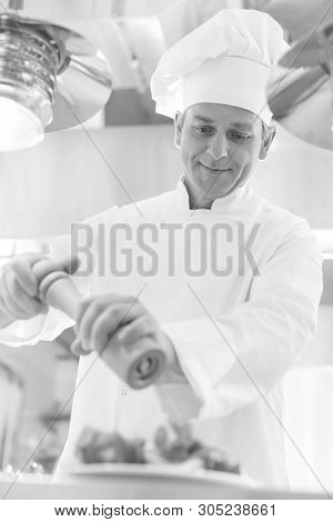 Black and White photo of Confident mature chef using peppermill on salad in plate at restaurant