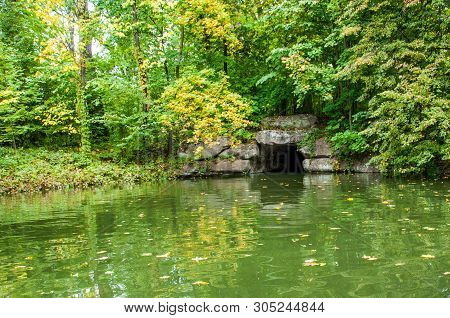 Ancient Stone Tunnel On Lake With Yellow Tree Leaves Fallen Into Calm Water. Reflection In Pond Wate