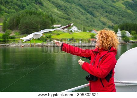 Young Woman Feeding Seagulls Flying Over The Ferry Boat. Woman In Red Jacket Traveling On Ferry Boat