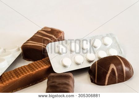 Chocolate Candies And Pills Lie On A White Table. Concept Of Dangerous Neighborhood Medicaments And 