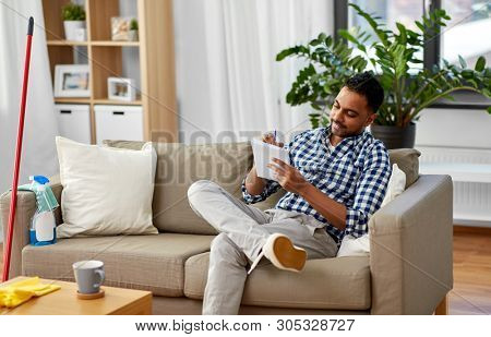 household and time management concept - smiling indian man making to do list in notebook after home cleaning