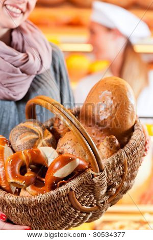 Kvindelige kunde stående med brødkurv og frisk brød og rundstykker i bageri