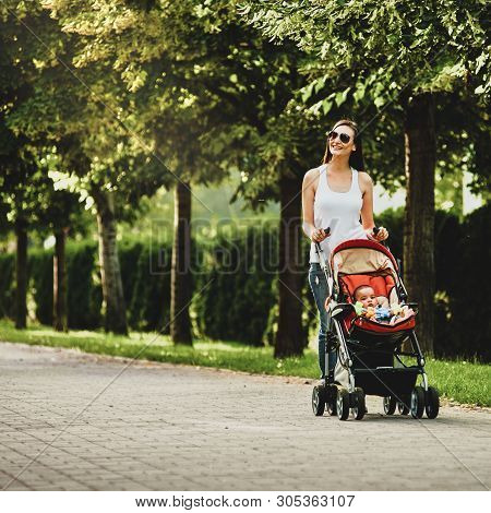 Happy Mother Walking With Babby Stroller In Summer Park