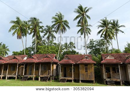Small Bungalows Near Palm Trees. Weathered Wooden Huts In Traditional Tropical Landscape. Rural Scen