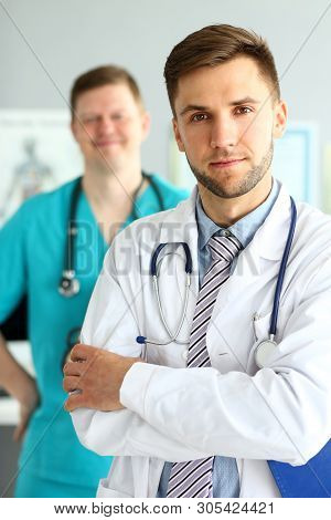 Portrait Of Handsome Man In White Uniform With Stethoscope. Smiling Doc Posing At Workplace In Clini
