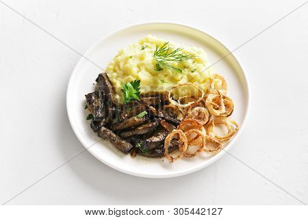 Close Up Of Roasted Beef Liver With Mashed Potatoes And Fried Onion Rings On White Plate Over Stone 