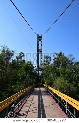 Suspension Bridge With Yellow Railings And Cables Across The River On Mount Kizilovka In The Foothil