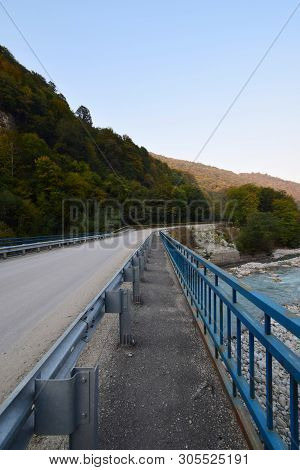 Mountain Road Across The River, With A Bridge With Blue Railings In The Cherek Gorge In The Mountain