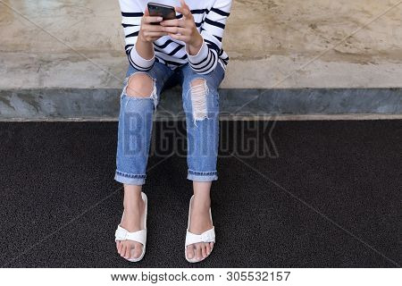 Woman In Rip Jeans Looks At Mobile Phone.