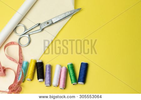 Sewing Accessories And Fabric On A Yelow Background. Sewing Threads, Pins, Pattern And Sewing Centim