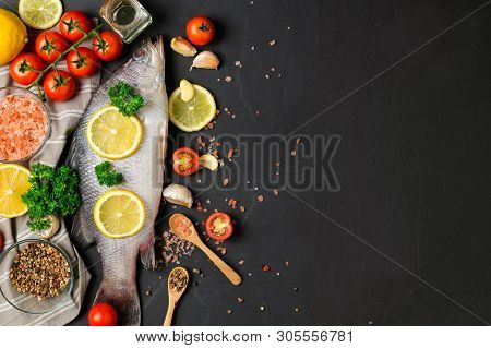 Fresh Fish Seabass And Ingredients For Cooking. Raw Fish Seabass With Spices And Herbs On Black Slat