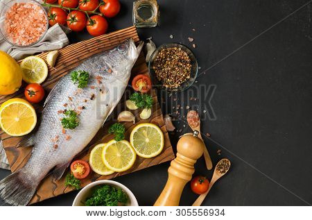 Fresh Fish Seabass And Ingredients For Cooking. Raw Fish Seabass With Spices And Herbs On Black Slat