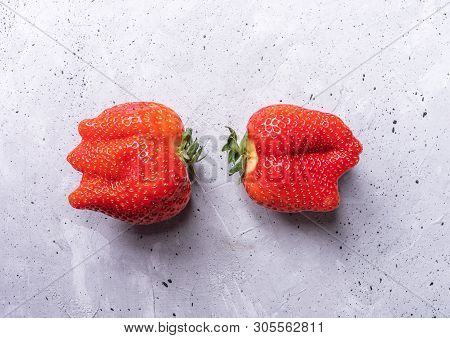 Two Ugly Strawberries Are Lying On Grey Concrete Background.