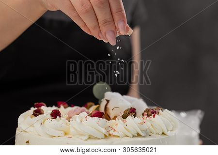 The Condater Sprinkles The Cake With Grated Almonds And Coconut. Close-up Of A Hand And Pouring Crum