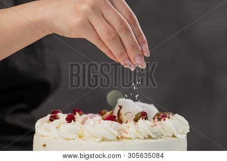 The Condater Sprinkles The Cake With Grated Almonds And Coconut. Close-up Of A Hand And Pouring Crum