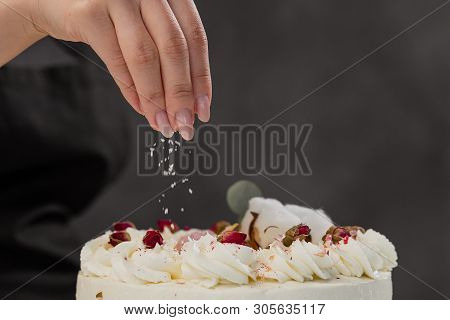 The Condater Sprinkles The Cake With Grated Almonds And Coconut. Close-up Of A Hand And Pouring Crum