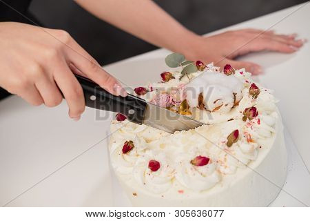 A Condater Cuts A Beautiful Fresh Decorated White Cake With A Large Knife.