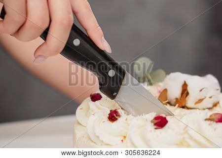 A Condater Cuts A Beautiful Fresh Decorated White Cake With A Large Knife.