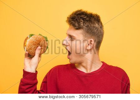 Hungry Guy Holds An Appetizing Burger In His Hands And Reacts Emotionally. Close Up Portrait Of A Su