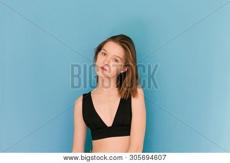 Girl Of Model Appearance On A Blue Background In A Bra, Looks Into The Camera And Poses On The Camer