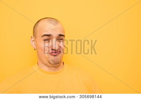 Funny Guy In Earrings And A Bald Head On His Head Wearing A Yellow Casual Dress, Makes A Funny Face 