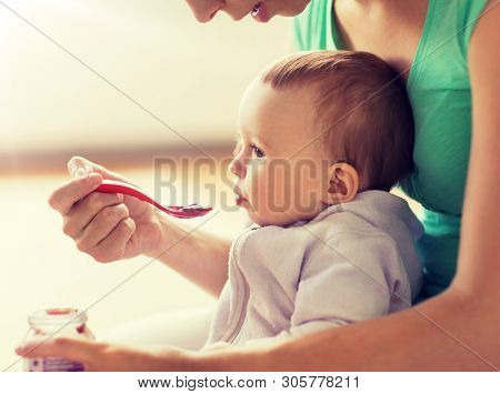 family, food, child, eating and parenthood concept - mother with puree and spoon feeding little baby at home