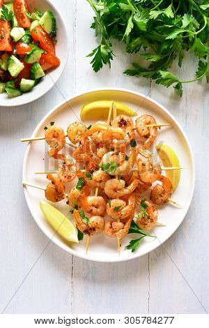 Grilled Shrimp Skewers. Prawns Skewers With Greens, Spices And Lemon On White Plate Over Wooden Tabl