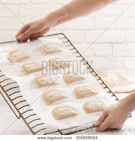 Woman put empanadillas , small filling tuna pies in roasting tray  to baked pastry in oven. Typical 
