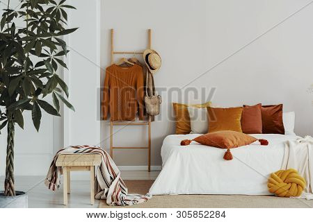 Sweaters, Wicker Hat And Bag On Wooden Ladder Next To King Size Bed With Velvet Pillows, Copy Space