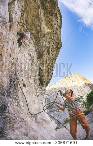 Athletic Man Climbs An Overhanging Rock 8c-9a Category With Rope With Man Belayed Him. Sport Climbin