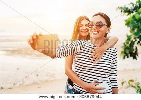 Two Caucasian Girlfriends Hugging And Posing For Selfie On The Sea Side Using Smartphone. Careless V